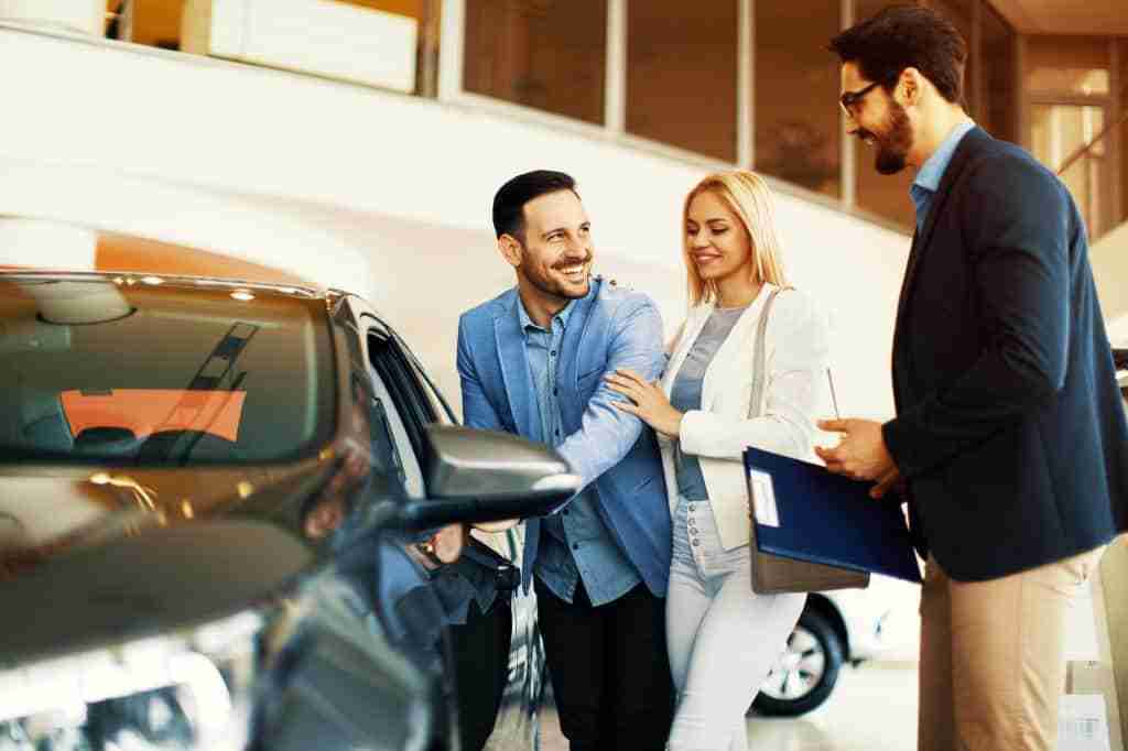 Happy Couple in Car Dealership with Car Salesmen