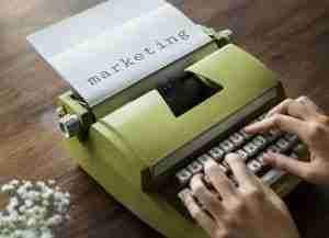 Person Typing On Typewriter with the word marketing already typed