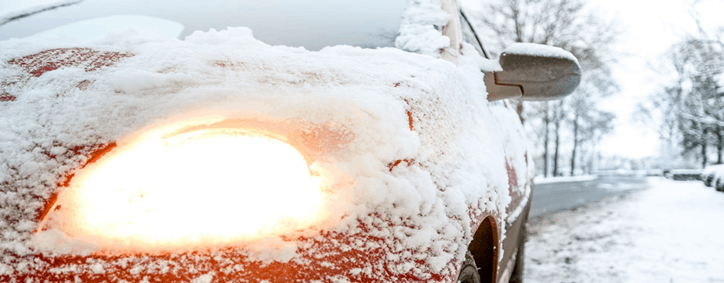 Red car frozen over in the snow with lights on.