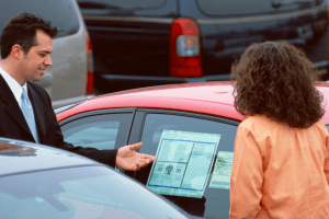 Car salesmen showing woman the window sticker of a new red car.