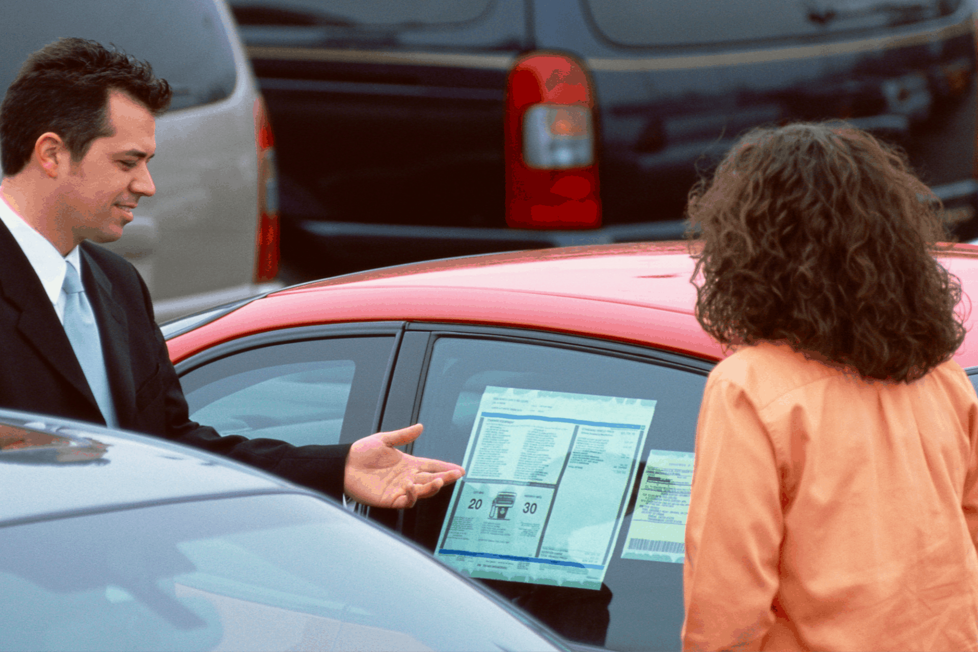 Car salesmen showing woman the window sticker of a new red car.